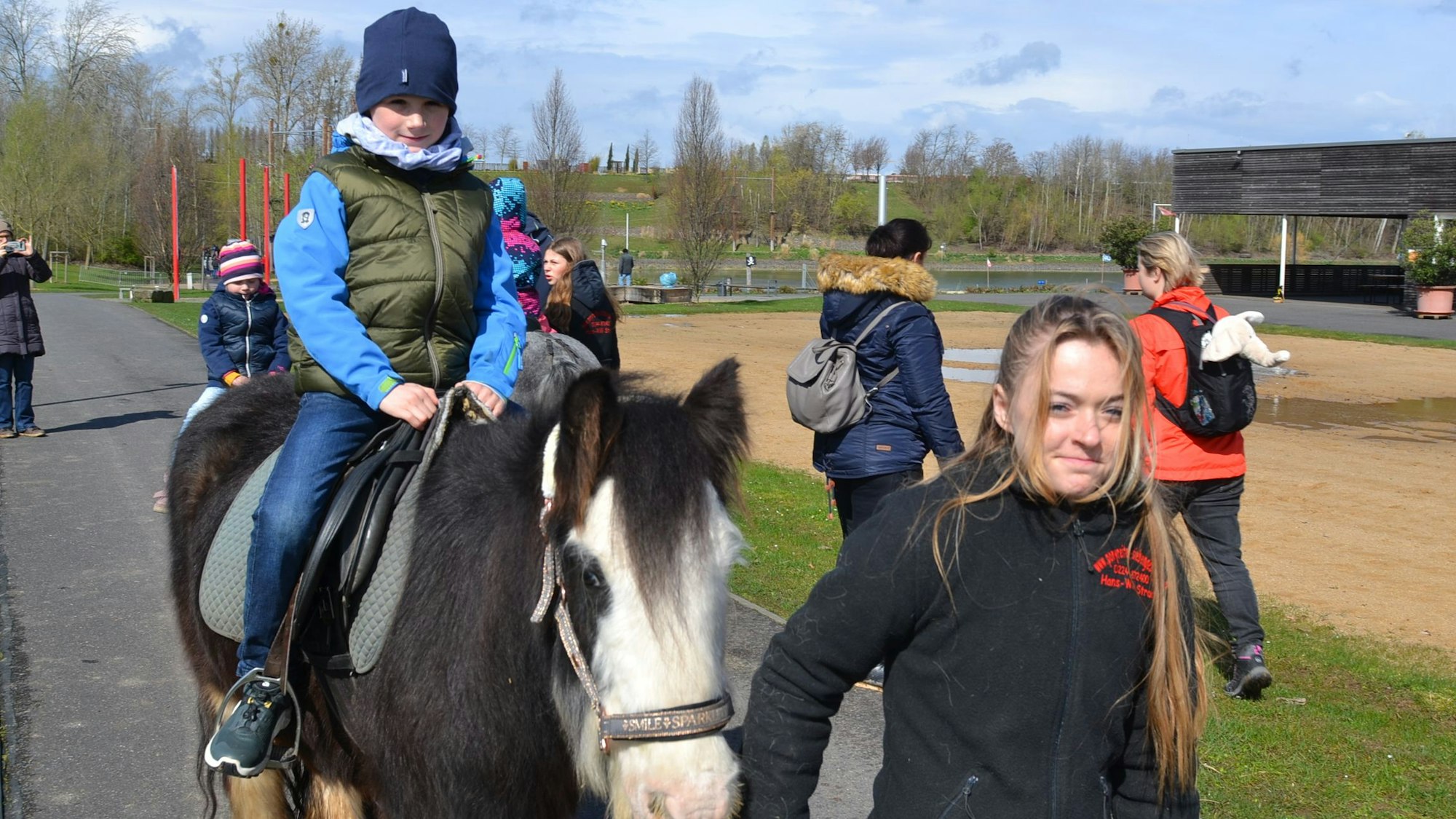 Auf einem Pony, das von einer Helferin geführt wird, ist ein Mädchen auf dem Gelände des Seeparks unterwegs.