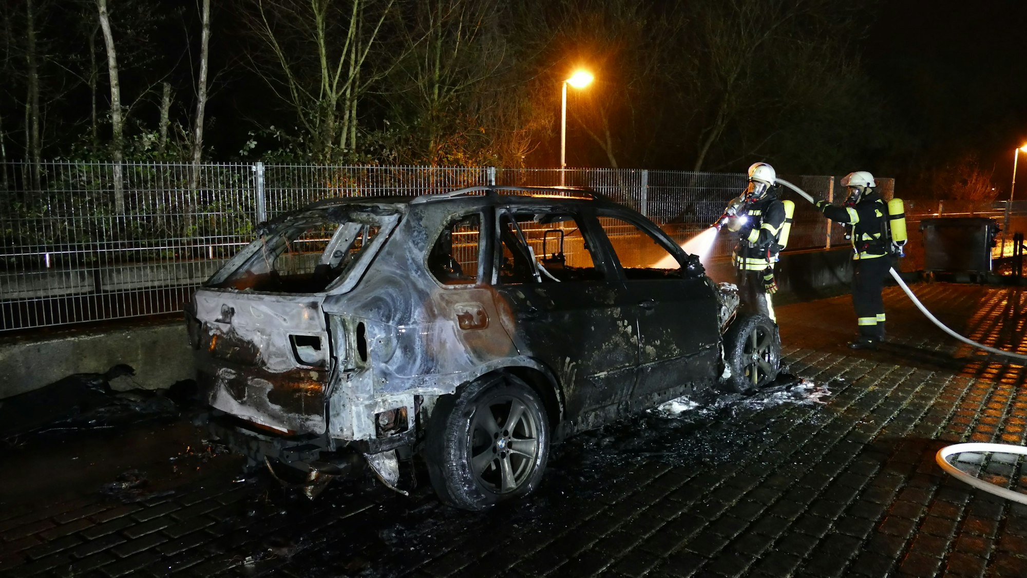 Feuerwehrleute löschen ein ausgebranntes Auto.