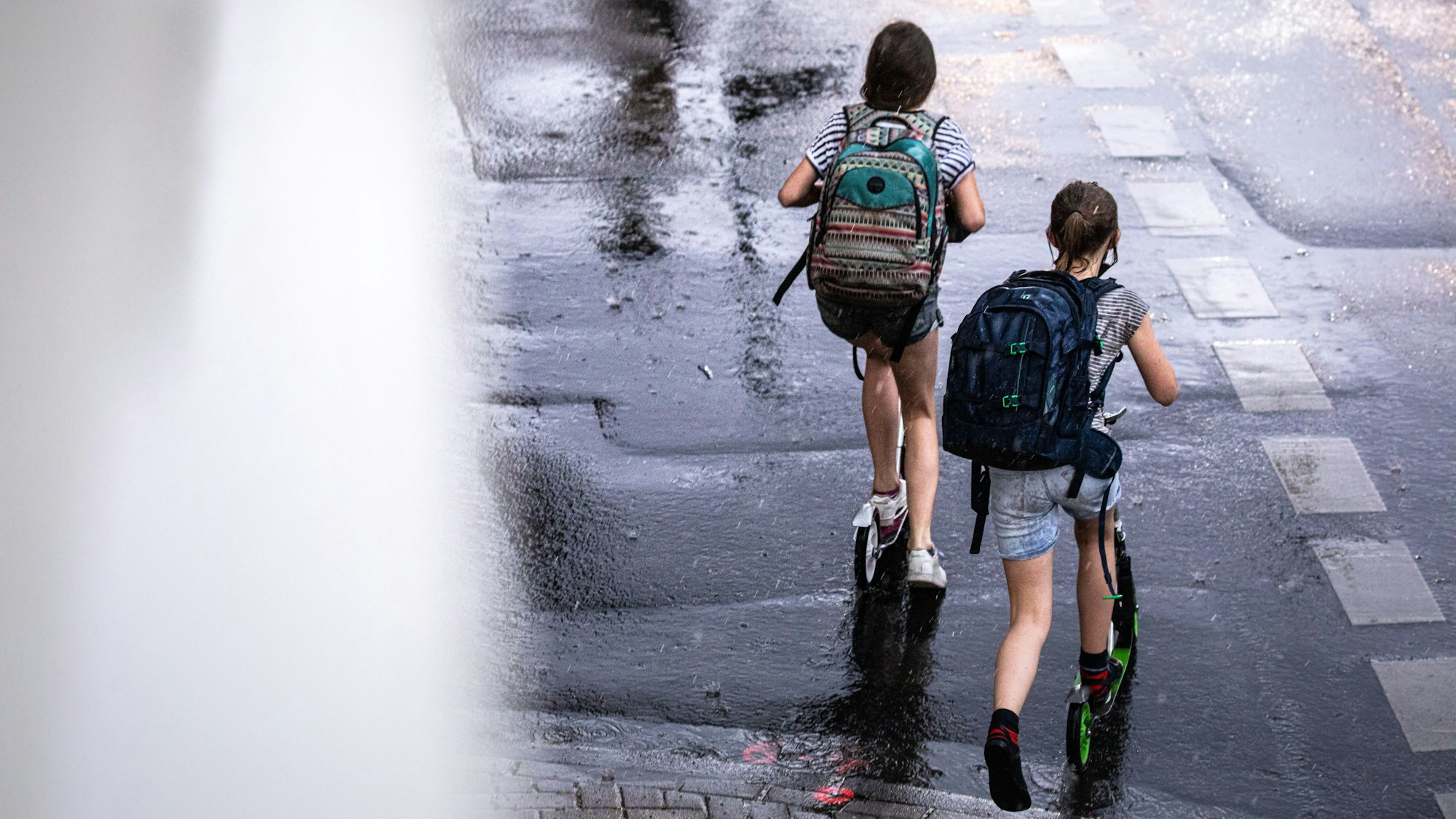 Zwei Schulkinder sind in Köln auf ihren Tretrollern unterwegs.