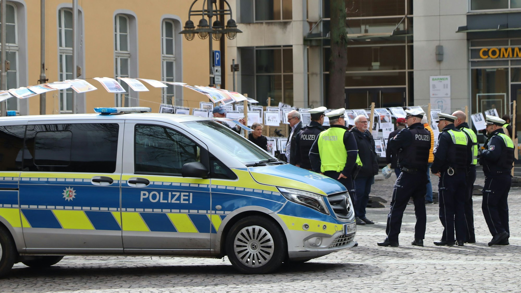Auf dem Foto sind Polizisten vor dem Brühler Rathaus zu sehen. Im Hintergrund sind die Fotos von Menschen aus Kriegsgebieten zu sehen.
