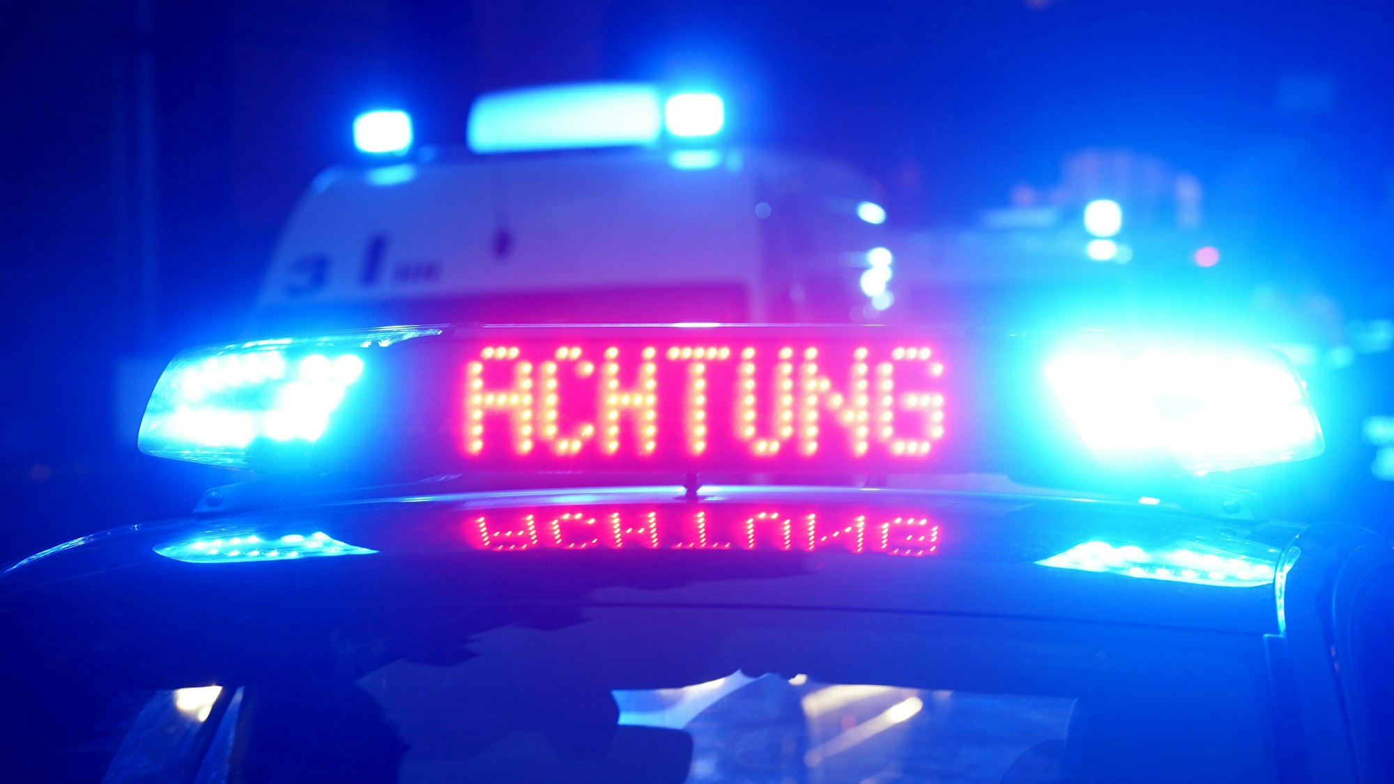 Das Bild zeigt einen Polizeiwagen in der Dunkelheit mit eingeschaltetem Blaulicht.