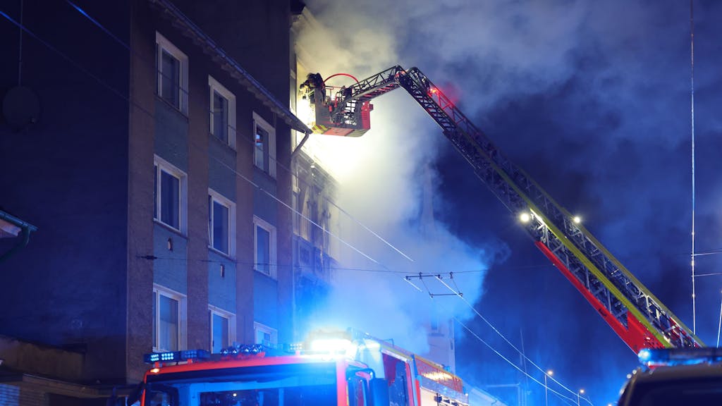 Von einer Drehleiter aus bekämpft ein Feuerwehrmann einen Brand in einem Mehrfamilienhaus. Bei dem Wohnungsbrand am frühen Montagmorgen (25. März 2024) sind vier Menschen getötet worden, darunter ein Kind.