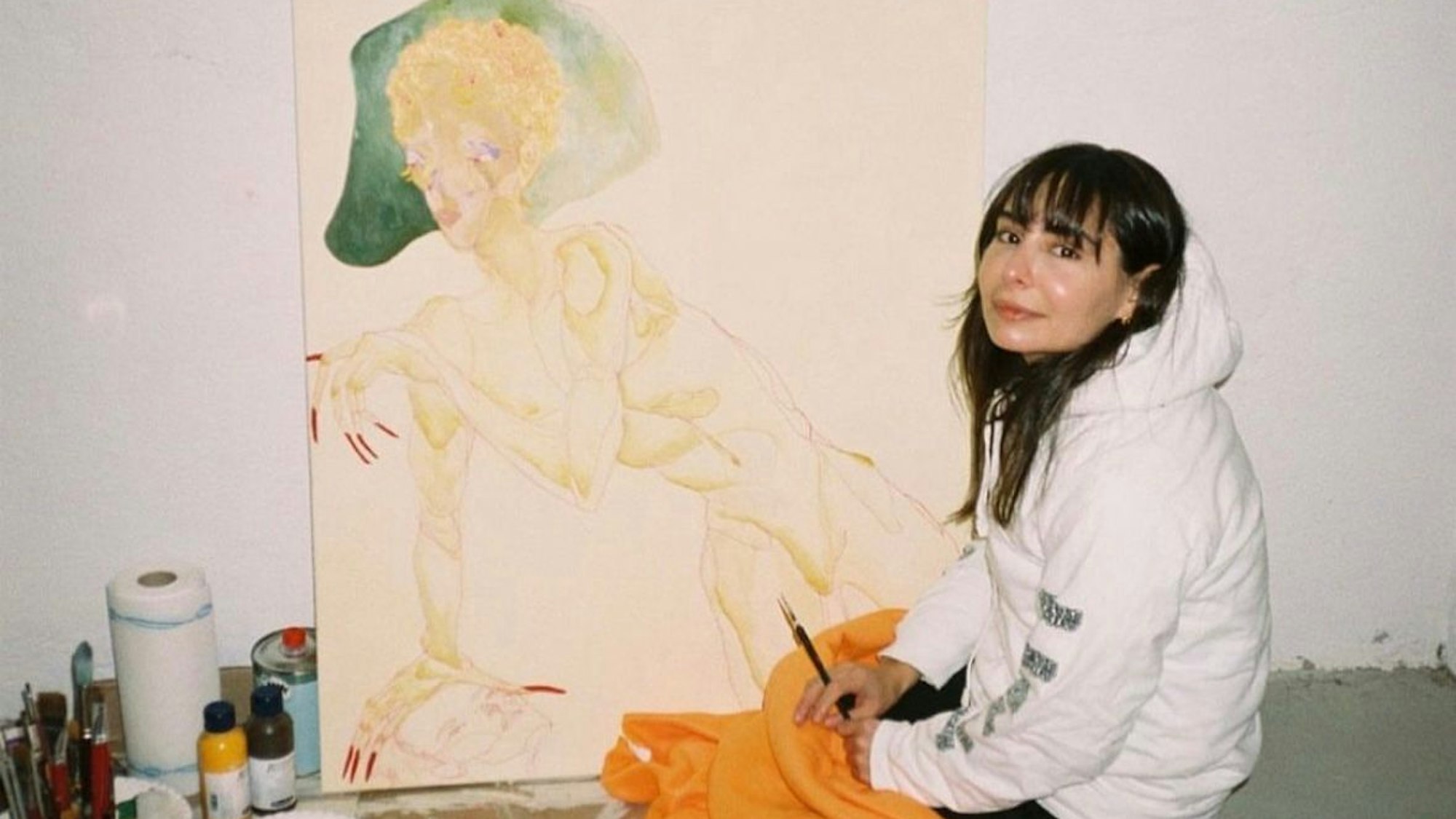 Die Künstlerin und Fotografin Zeliha Cambaz sitzt vor einem ihrer Gemälde.