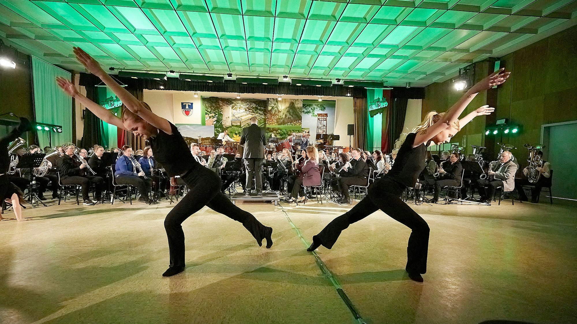 Zwei Tänzerinnen sind im Vordergrund und das Orchester im Hintergrund zu sehen.