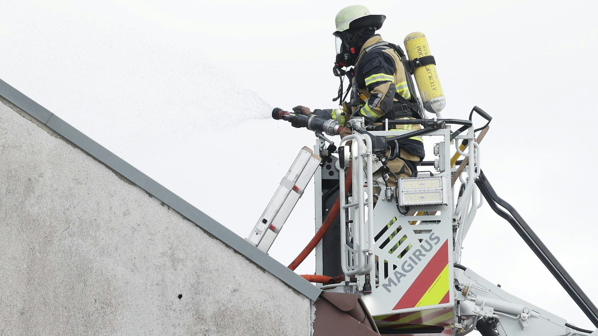 Solingen: Ein Feuerwehrmann steht an einem Mehrfamilienhaus, in dem es gebrannt hat, im Korb einer Drehleiter und bekämpft Brandnester.