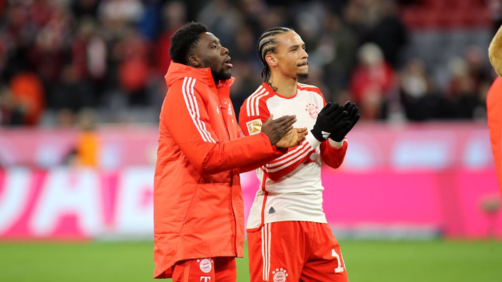 Alphonso Davies und Leroy Sané stehen vor der Kurve der Fans des FC Bayern.
