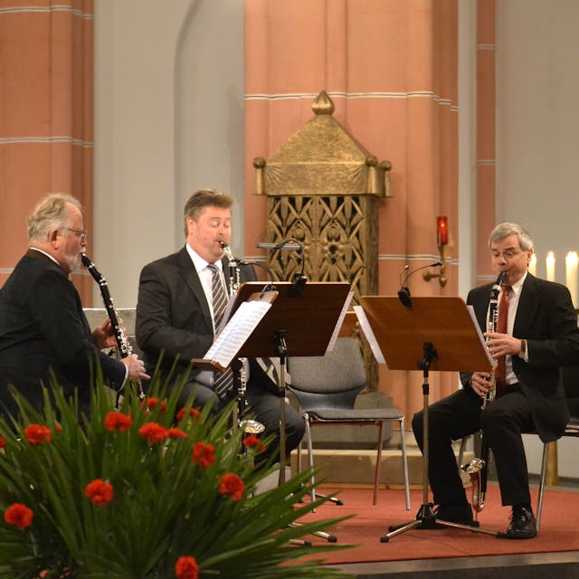 Drei Instrumentalisten musizieren vor dem Altar in der Euskirchener Herz-Jesu-Kirche. Im Vordergrund Blumen, im Hintergrund Kerzen.