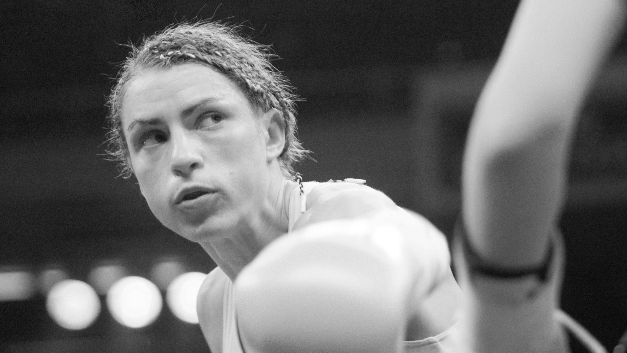 Die Schwarz-weiß-Aufnahme zeigt Aesia Graf mit angespanntem Gesicht gegenüber eine Kontrahentin im Boxring.