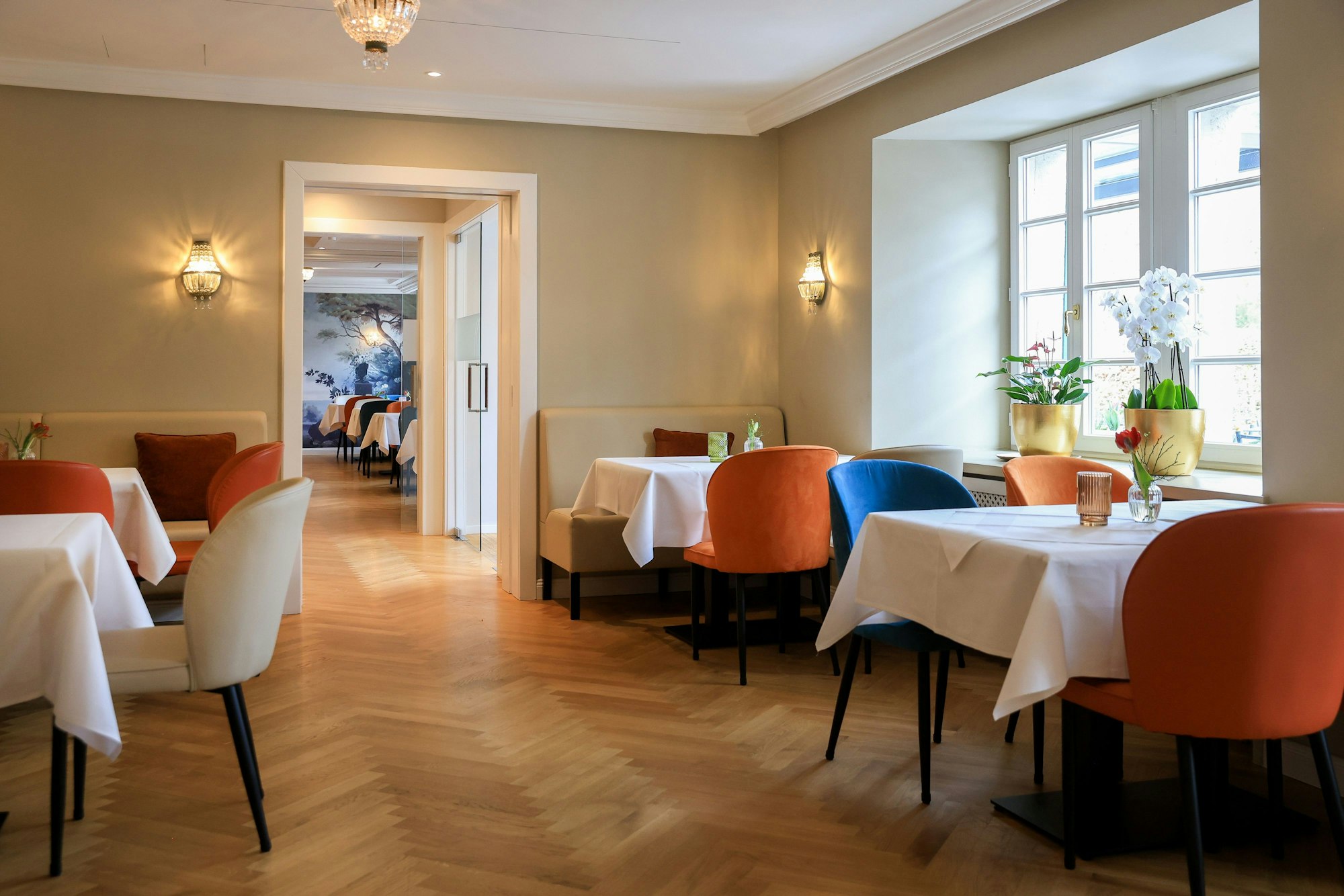 Das Restaurant von innen, die Tische sind mit weißen Tischdecken bedeckt und die Stühle in bunten Farben mit Samt bezogen
