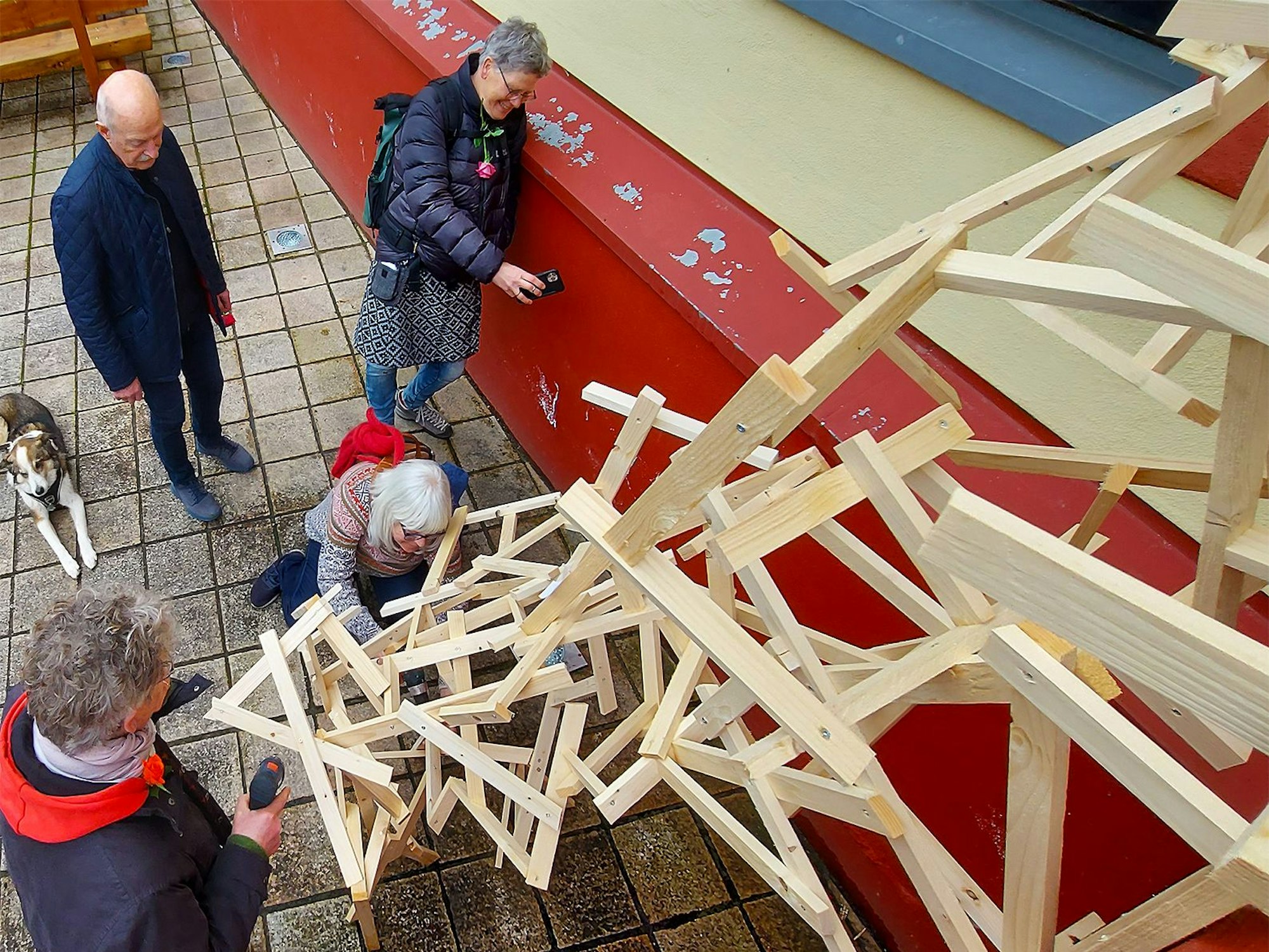 Vier Personen stehen an einer Holzkonstruktion, die die Besucher der aktuellen Ausstellung im Kunstforum in Gemünd gemeinsam gestalteten.