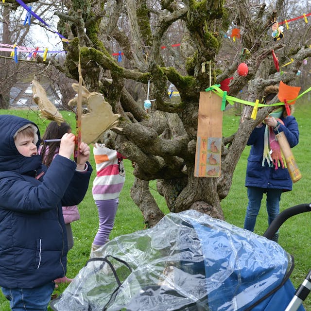 An einem knorrigen Baum hat ein Kind mit einer Wäscheklammer einen Zettel an einer Schnur befestigt. Darauf schreibt es seine Wünsche.
