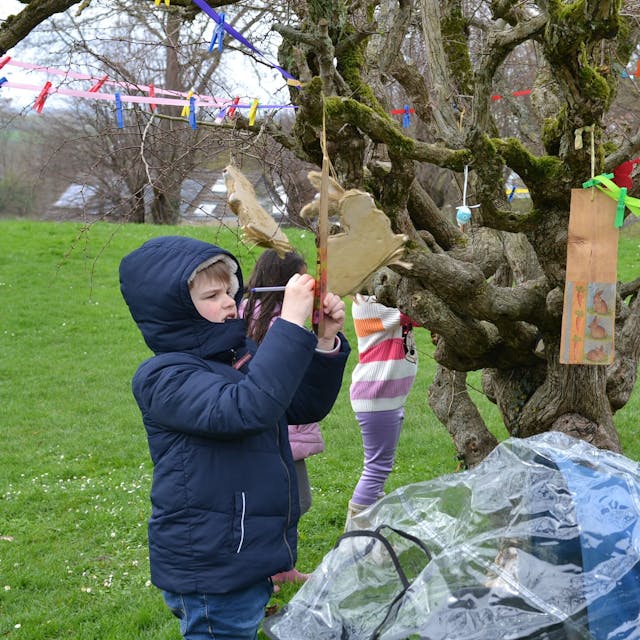 An einem knorrigen Baum hat ein Kind mit einer Wäscheklammer einen Zettel an einer Schnur befestigt. Darauf schreibt es seine Wünsche.