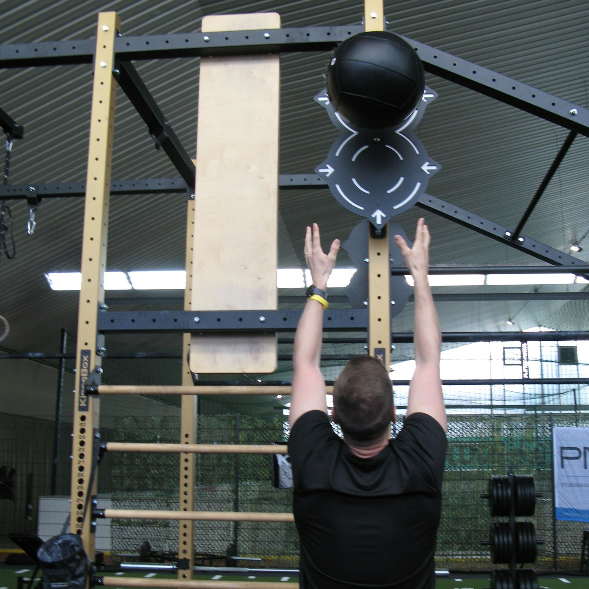 Der Hyrox-Sportler Roman Hopp wirft einen Medizinball gegen ein in drei Metern Höhe angebrachtes Schild.