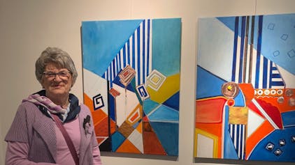 Eine Frau steht neben zwei farbigen Kunstwerken.
