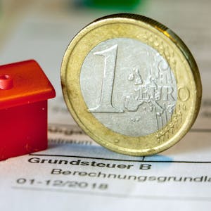 &nbsp;Eine Euro-Geldmünze sowie ein Spielzeughaus stehen auf einem Abgabenbescheid für die Entrichtung der Grundsteuer.&nbsp;