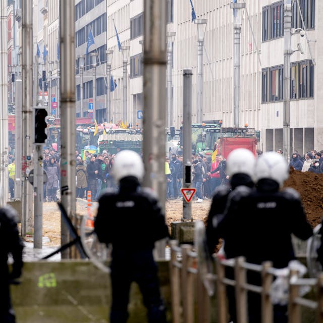 Brüssel: Polizisten patrouillieren hinter einer Absperrung, während Landwirte vor dem Gebäude des Europäischen Rates protestieren.