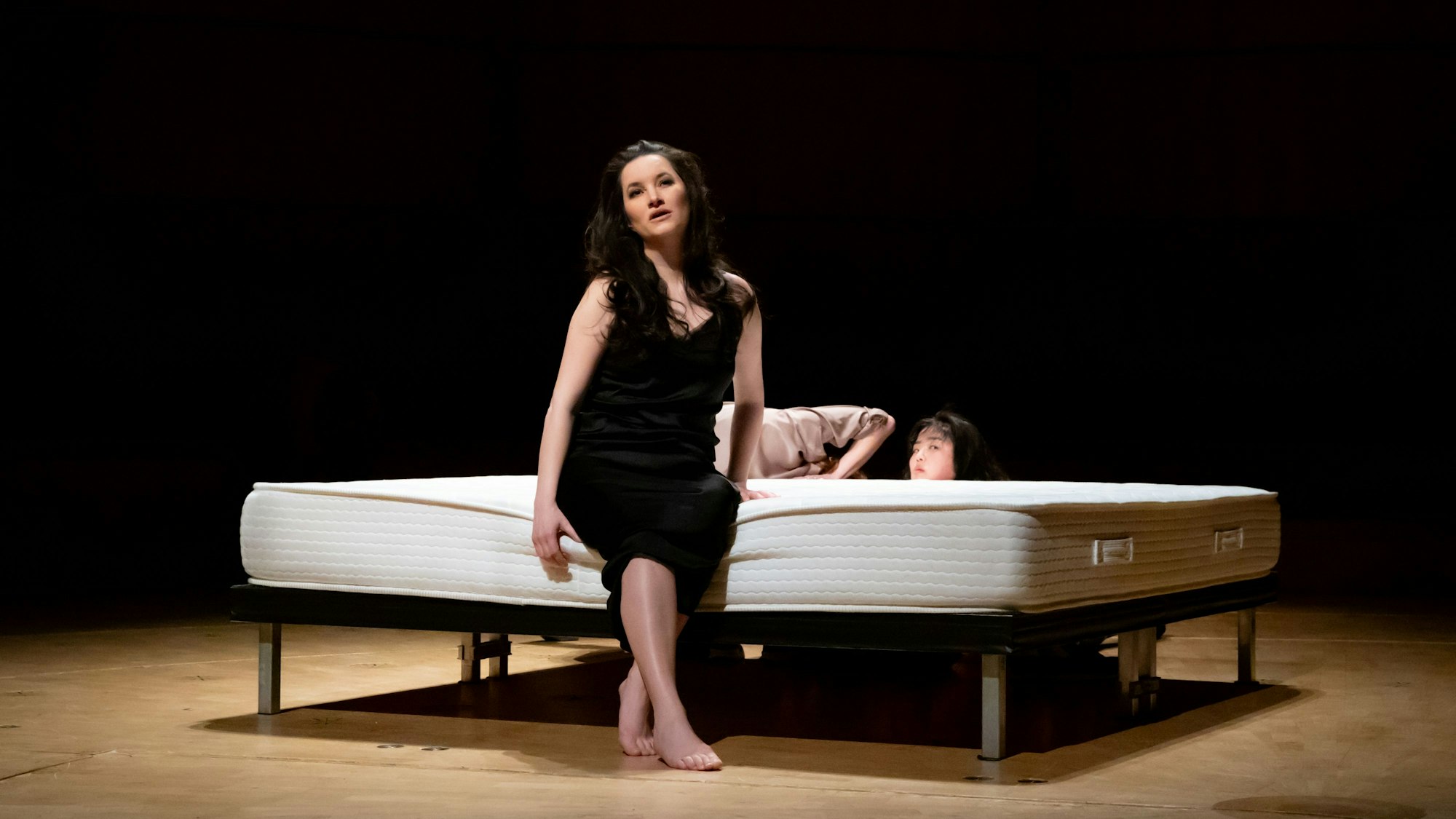 Die Sopranistin Anna Prohaska sitzt auf dem einzigen Objekt auf der Bühne, einer nackten Doppelmatratze auf niedrigem Gestell.