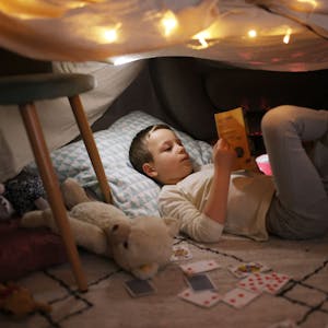 Ein Junge liegt in einer selbstgebauten Höhle mit Sternenhimmel und liest ein Buch.