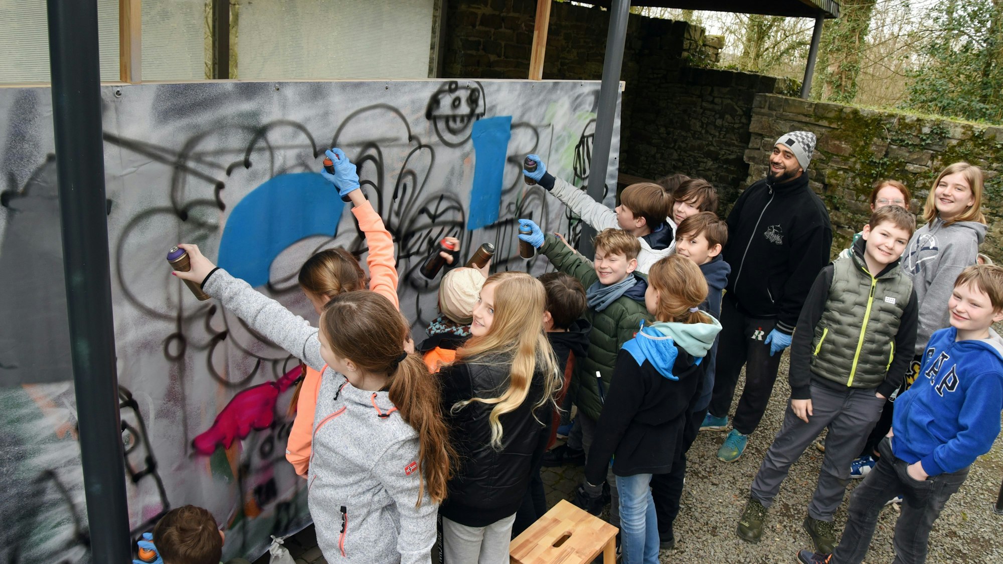 Mehrere Jugendliche sprühen gemeinsam ein Graffito auf eine Leinwand.
