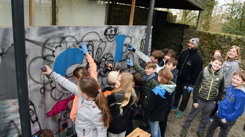 Mehrere Jugendliche sprühen gemeinsam ein Graffito auf eine Leinwand.&nbsp;