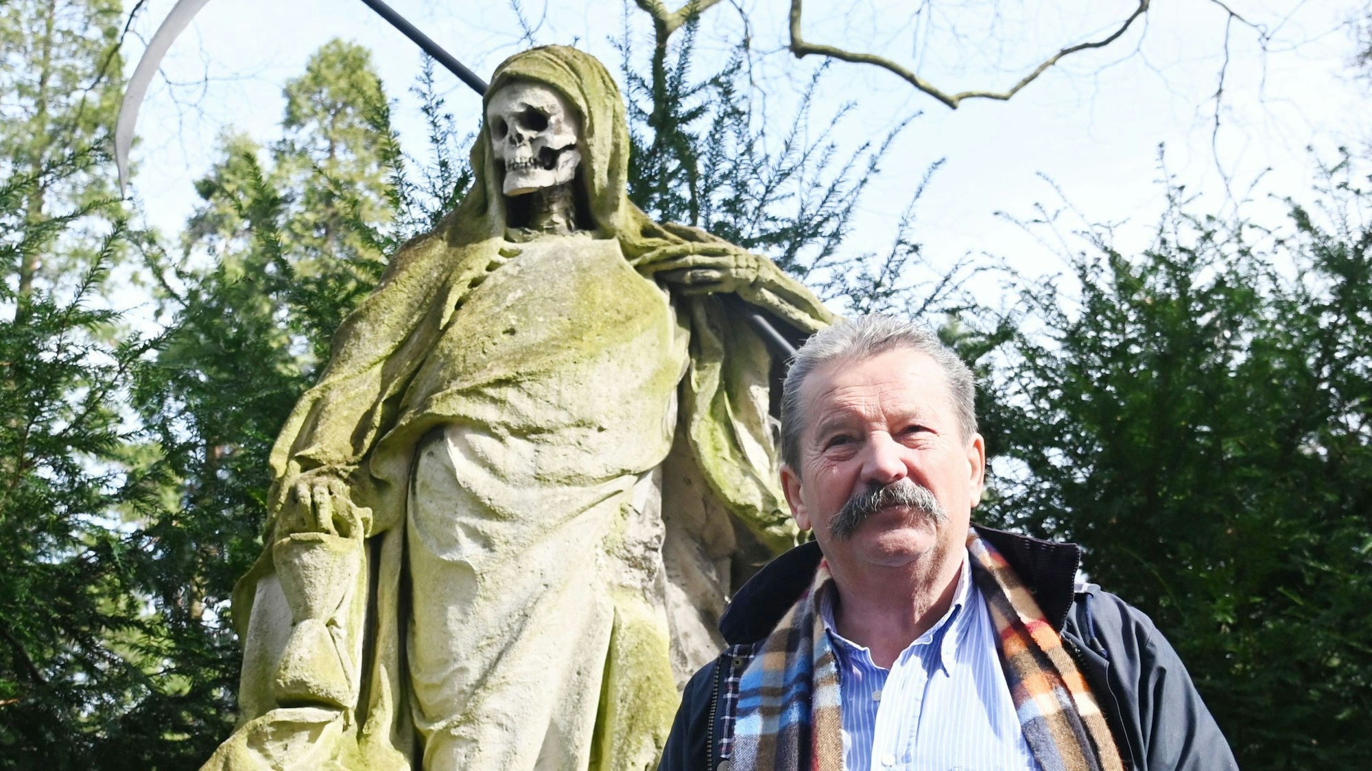 Porträt von Friedhofsleiter vor einer Skulptur des Sensenmannes.