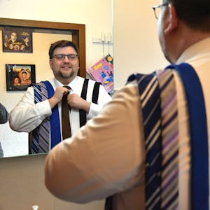 Martin Ahmann steht vor einem Spiegel und bindet eine Krawatte.