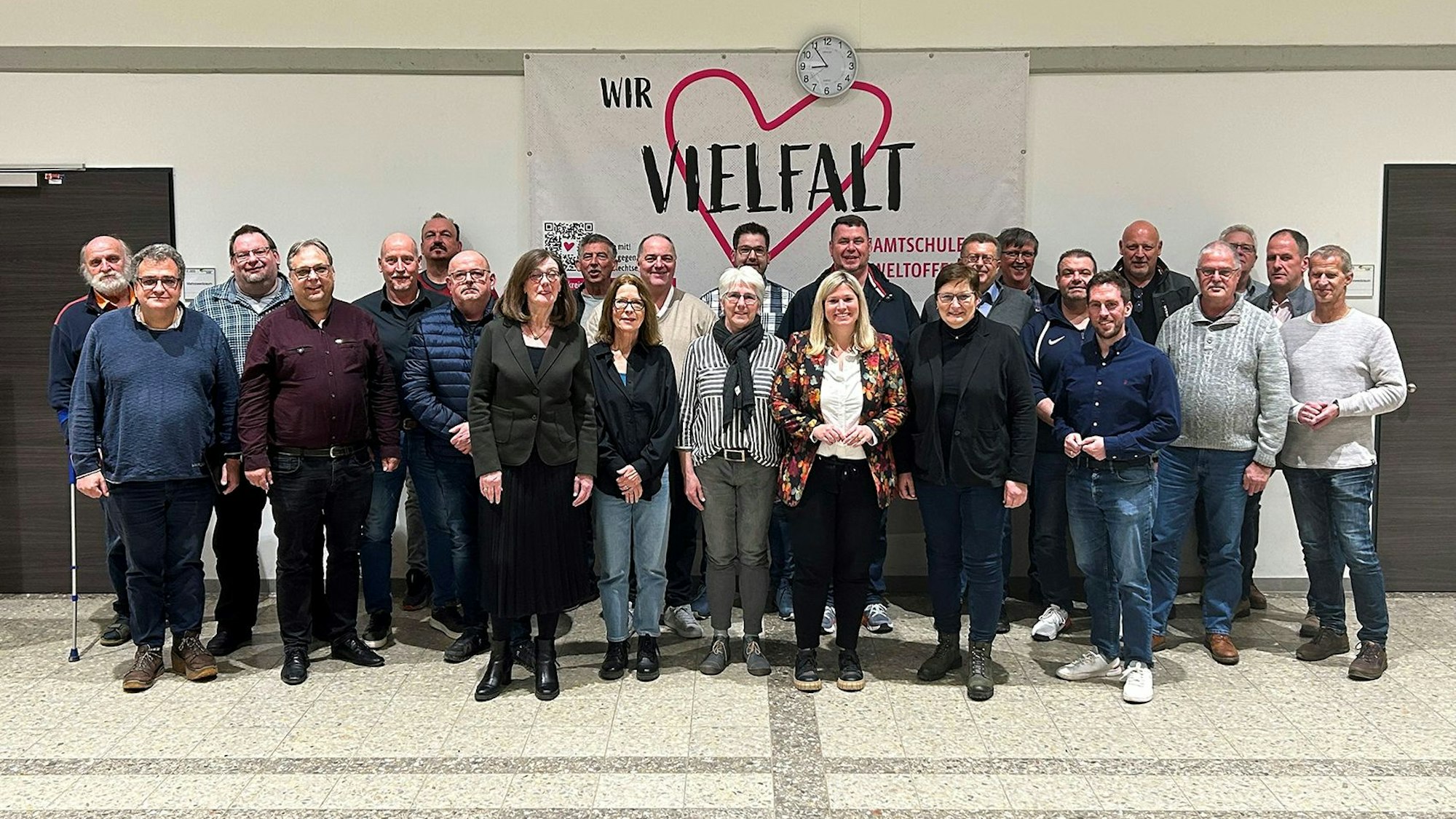 Zahlreiche Frauen und Männer aus der Gemeinde Blankenheim stehen vor einem Plakat, das ein rotes Herz zeigt mit dem Schriftzug „Vielfalt“.