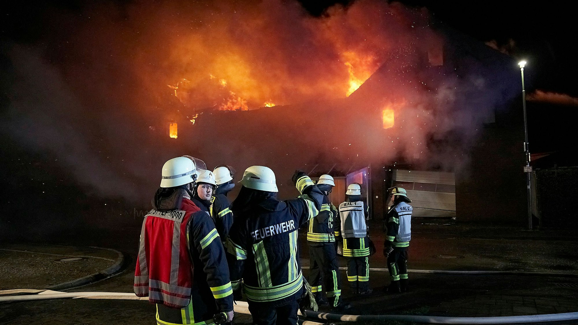 Einige Feuerwehrleute stehen vor einem brennenden Haus in Schleiden-Herhahn.