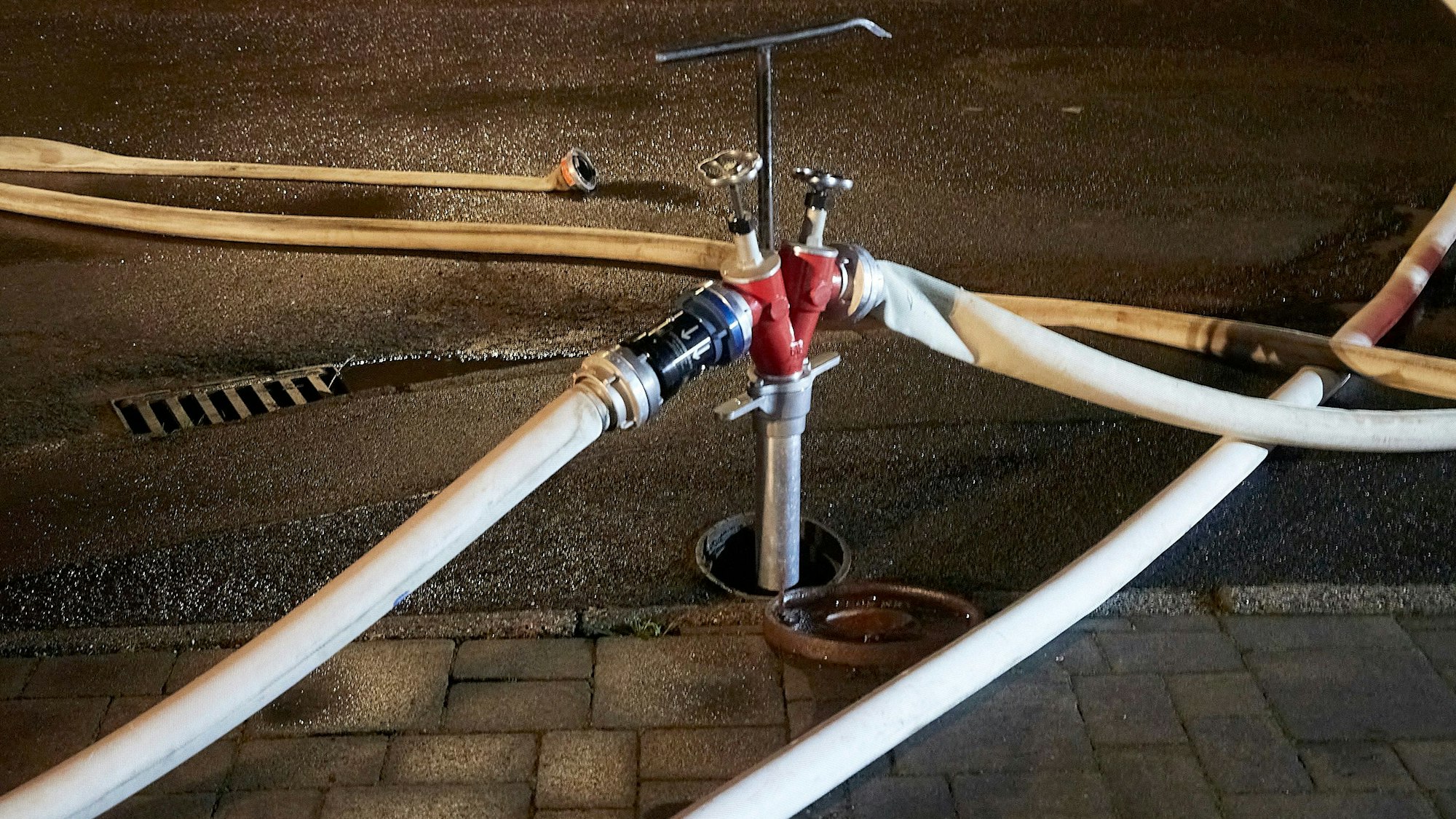 An einem Hydranten in einer Straße in Herhahn sind über ein Standrohr zwei Feuerwehrschläuche angeschlossen.