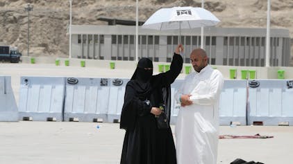 Eine Frau hält einen Schirm über einen Mann  der sein Gebet am letzten Tag der Hadsch in Mekka in Saudi-Arabien verrichtet.
