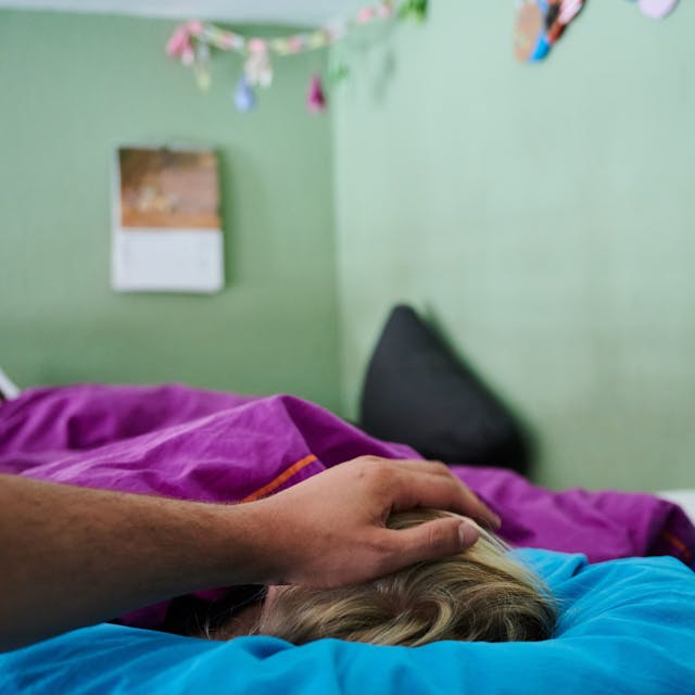 Ein Vater legt seine Hand auf den Kopf eines Kindes, das im Bett liegt. (Symbolbild)