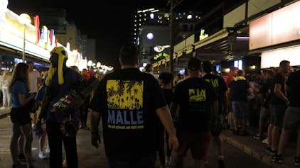 Männer, die ein T-Shirt mit der Aufschrift „Malle“ tragen, gehen durch die Schinkenstraße im so genannten Ballermann-Viertel auf Mallorca, hier im Mai 2022.