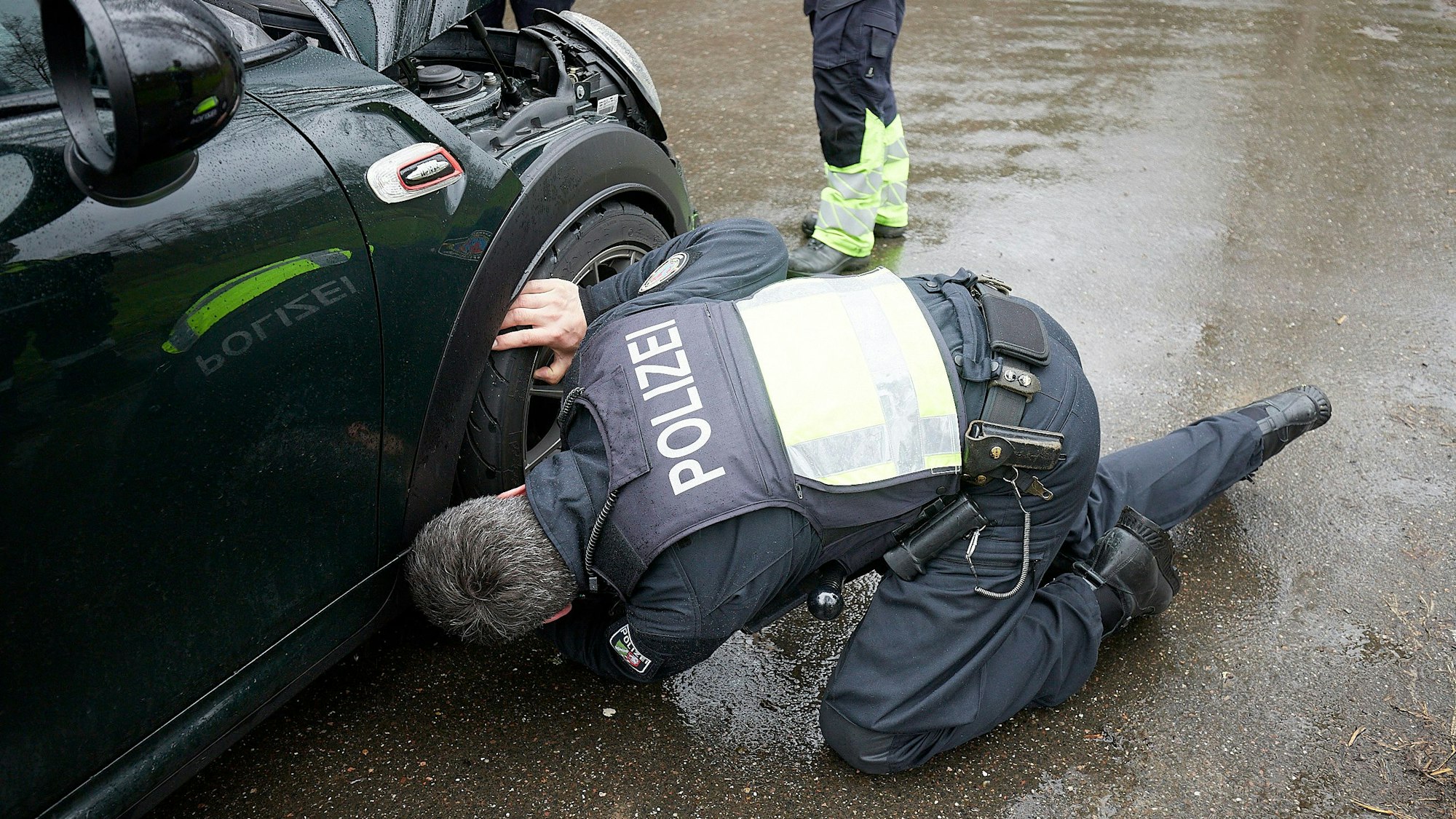 Ein Polizist kniet an einem Sportwagen und kontrolliert die Reifen.