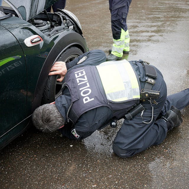 Ein Polizist kniet an einem Sportwagen und kontrolliert die Reifen.