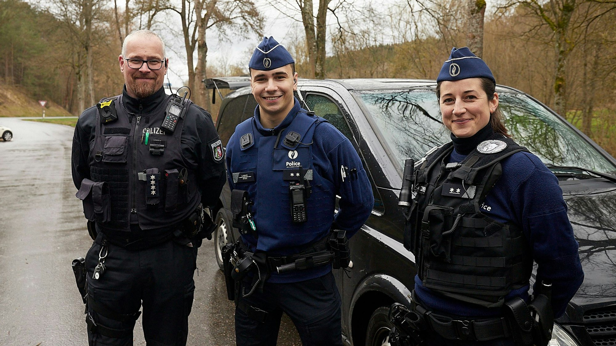 Zwei belgische Polizisten und ein deutscher Polizist stehen zusammen an einem Auto.