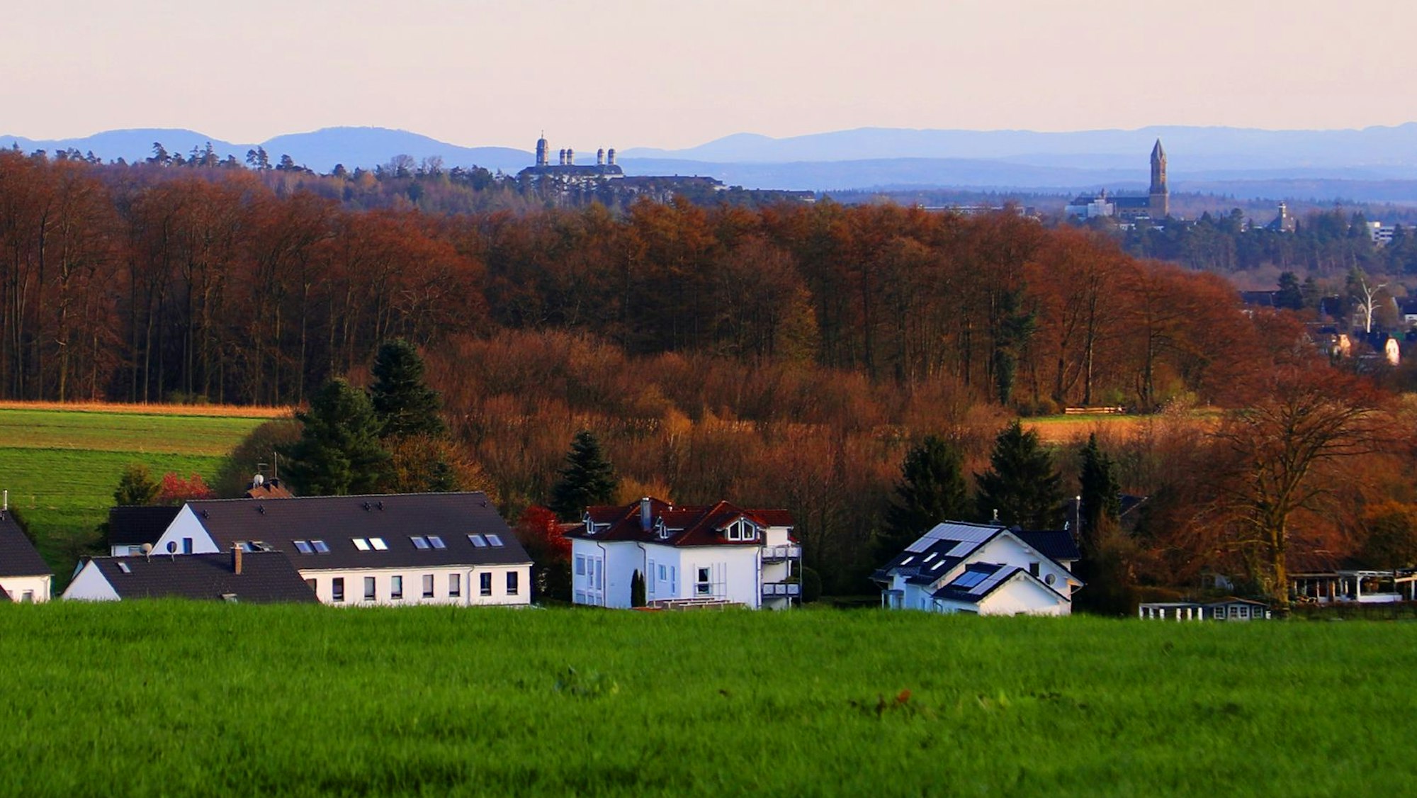 Am Horizont eines Landschaftsbildes sind Schlosstürme und eine Kirche sowie Berge in der Ferne zu sehen.