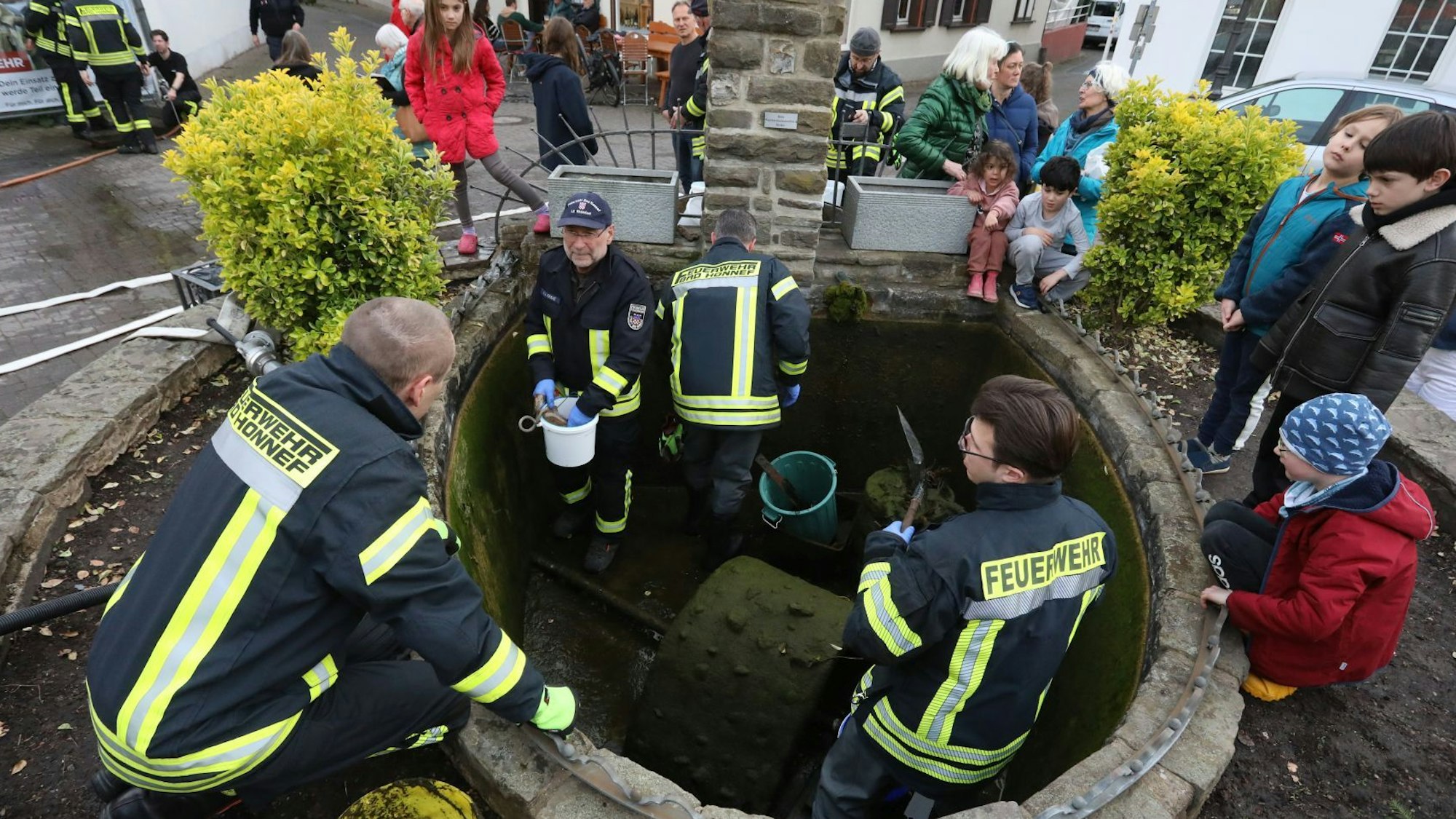 Vier Feuerwehrleute stehen in einem leeren Brunnenbecken, am Rand schau Menschen zu.