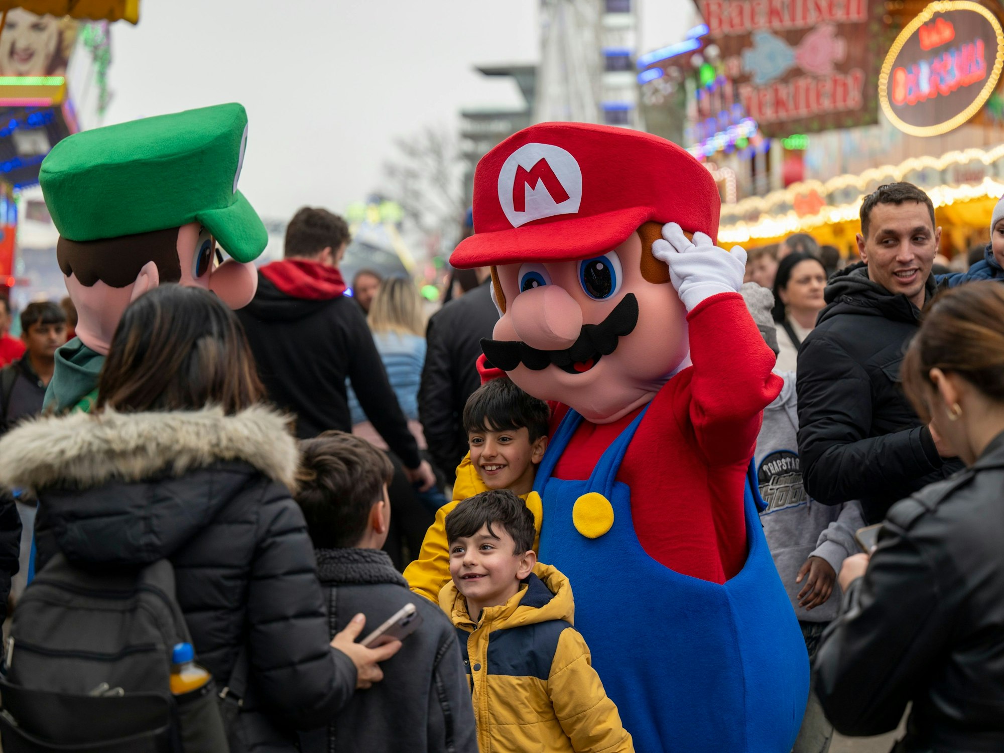 Ein Mensch in einem Kostüm mit Latzhose und roter Mütze drückt zwei kleine Jungs an sich.