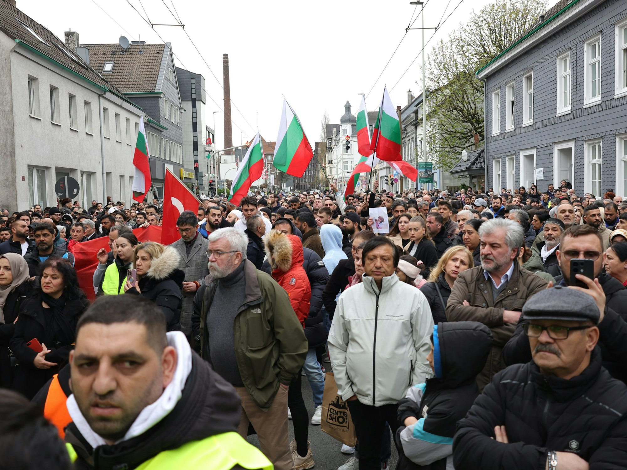 Mit bulgarischen und deutschen Flaggen ziehen Teilnehmende am Samstag, 30. März 2024, von der Innenstadt zu dem ausgebrannten Haus, in dem eine aus Bulgarien stammende Familie ums Leben kam.