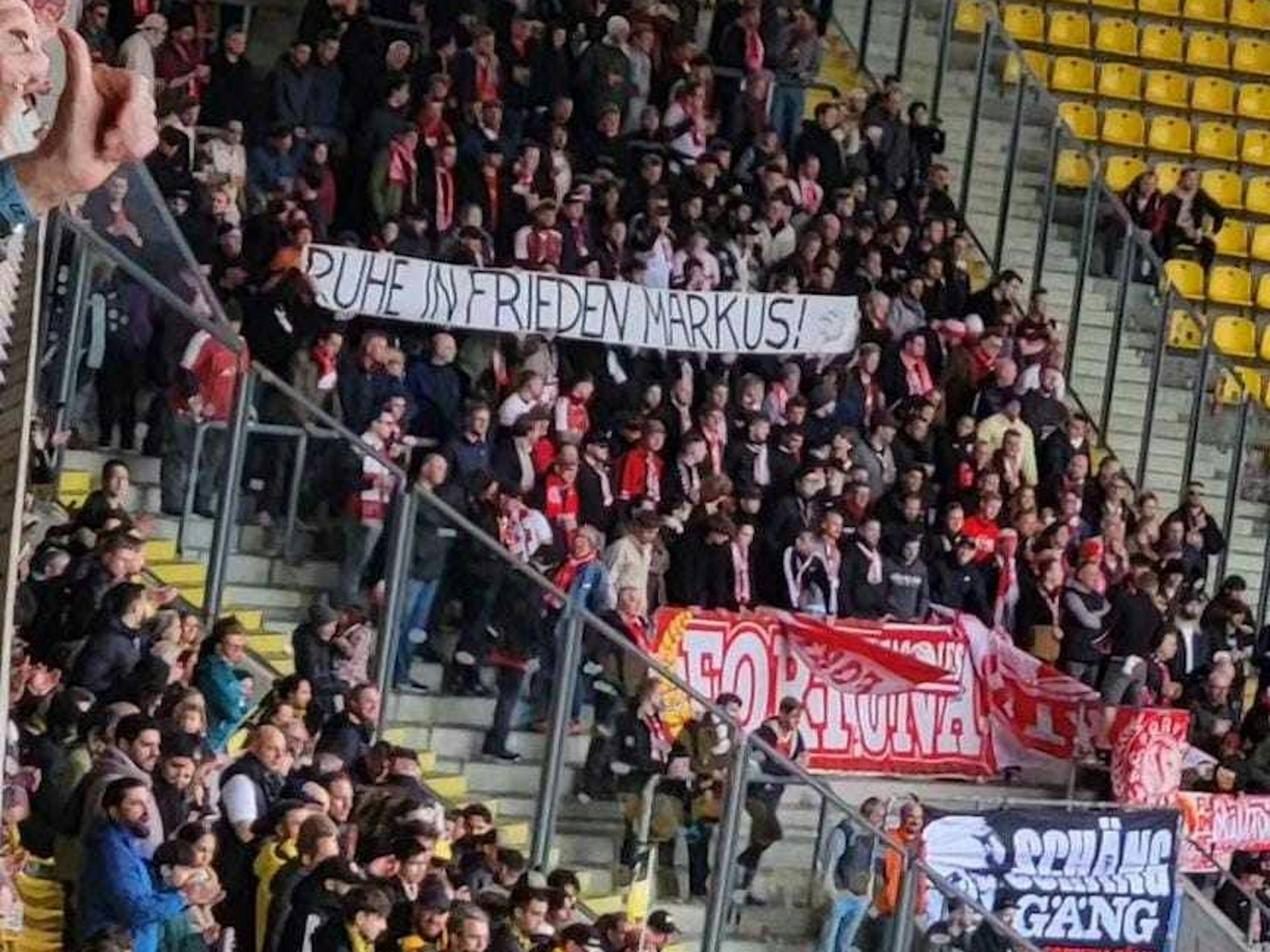 In einem Stadion halten Fans im Zuschauerblock ein Banner mit der Aufschrift „Ruhe in Frieden Markus!“ hoch.