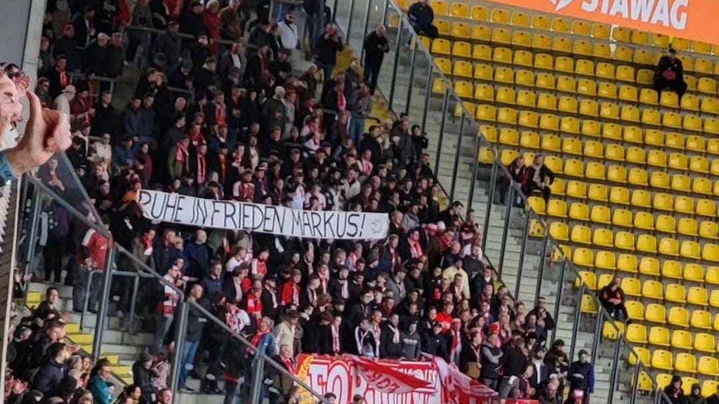 In einem Stadion halten Fans im Zuschauerblock ein Banner mit der Aufschrift „Ruhe in Frieden Markus!“ hoch.&nbsp;