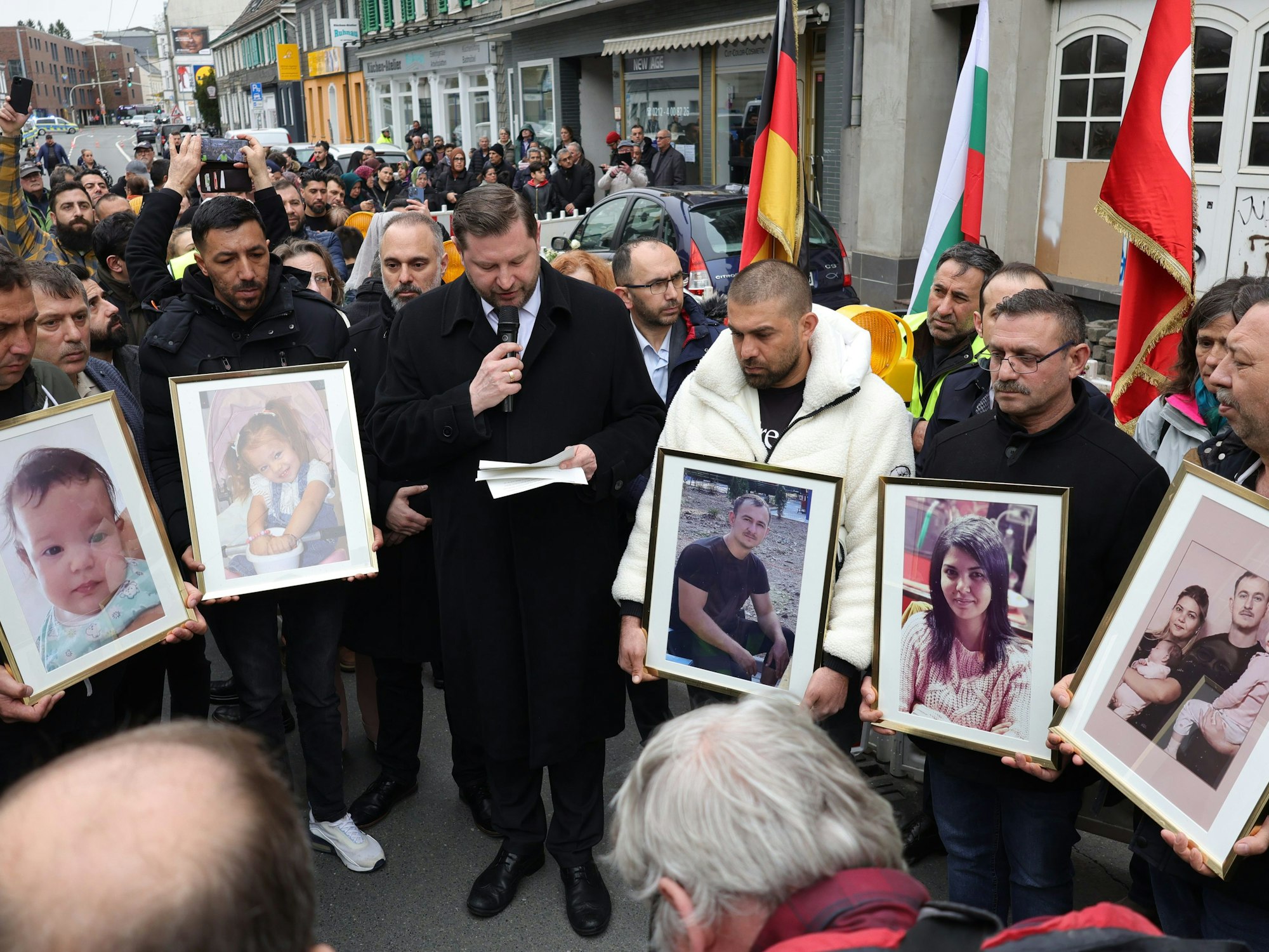 Tim Kurzbach (SPD, Mitte), Oberbürgermeister von Solingen, hält am Samstag (30. März 2024) eine Ansprache neben Männern, die Fotos der aus Bulgarien stammende Familie zeigen.