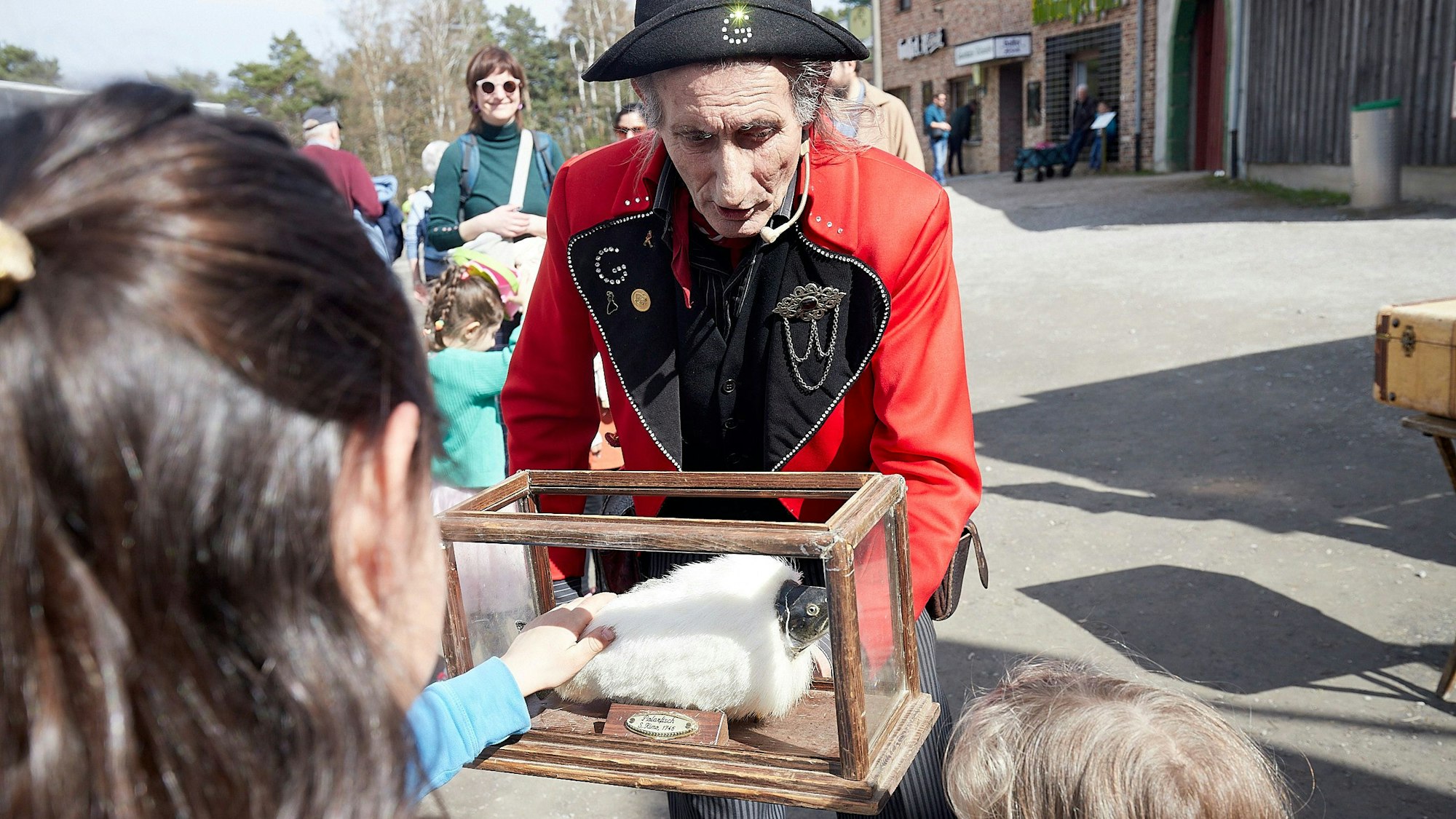 Ein in französischer Uniform gekleideter Mann präsentiert Kindern ein Stofftier in einem Glaskasten.
