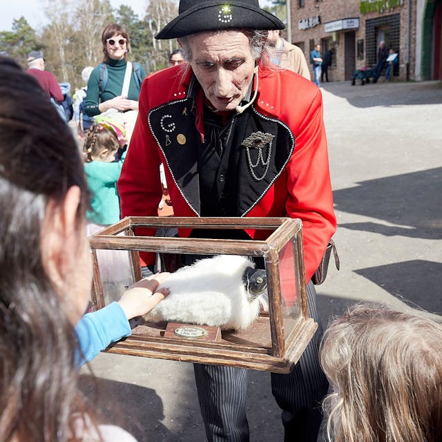 Ein in französischer Uniform gekleideter Mann präsentiert Kindern ein Stofftier in einem Glaskasten.&nbsp;