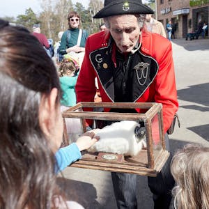 Ein in französischer Uniform gekleideter Mann präsentiert Kindern ein Stofftier in einem Glaskasten.&nbsp;