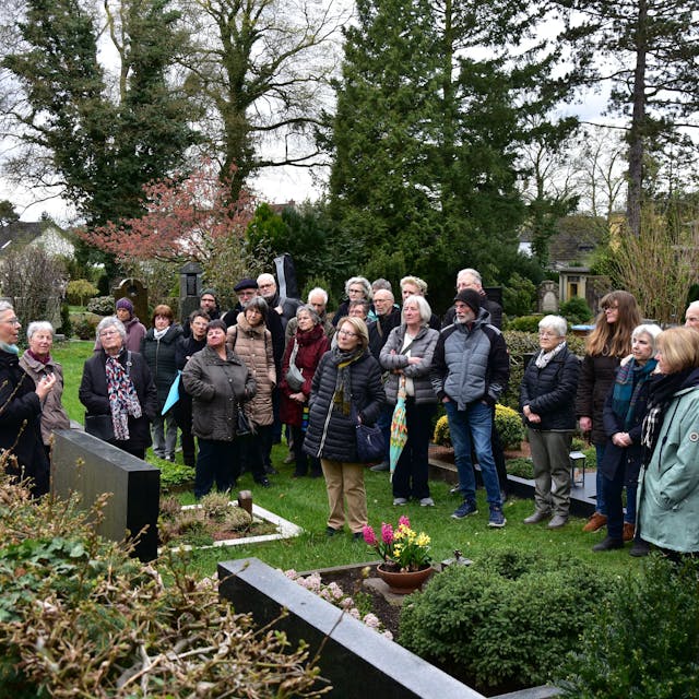 Eine Gruppe von Menschen steht vor Gräbern auf dem Friedhof.