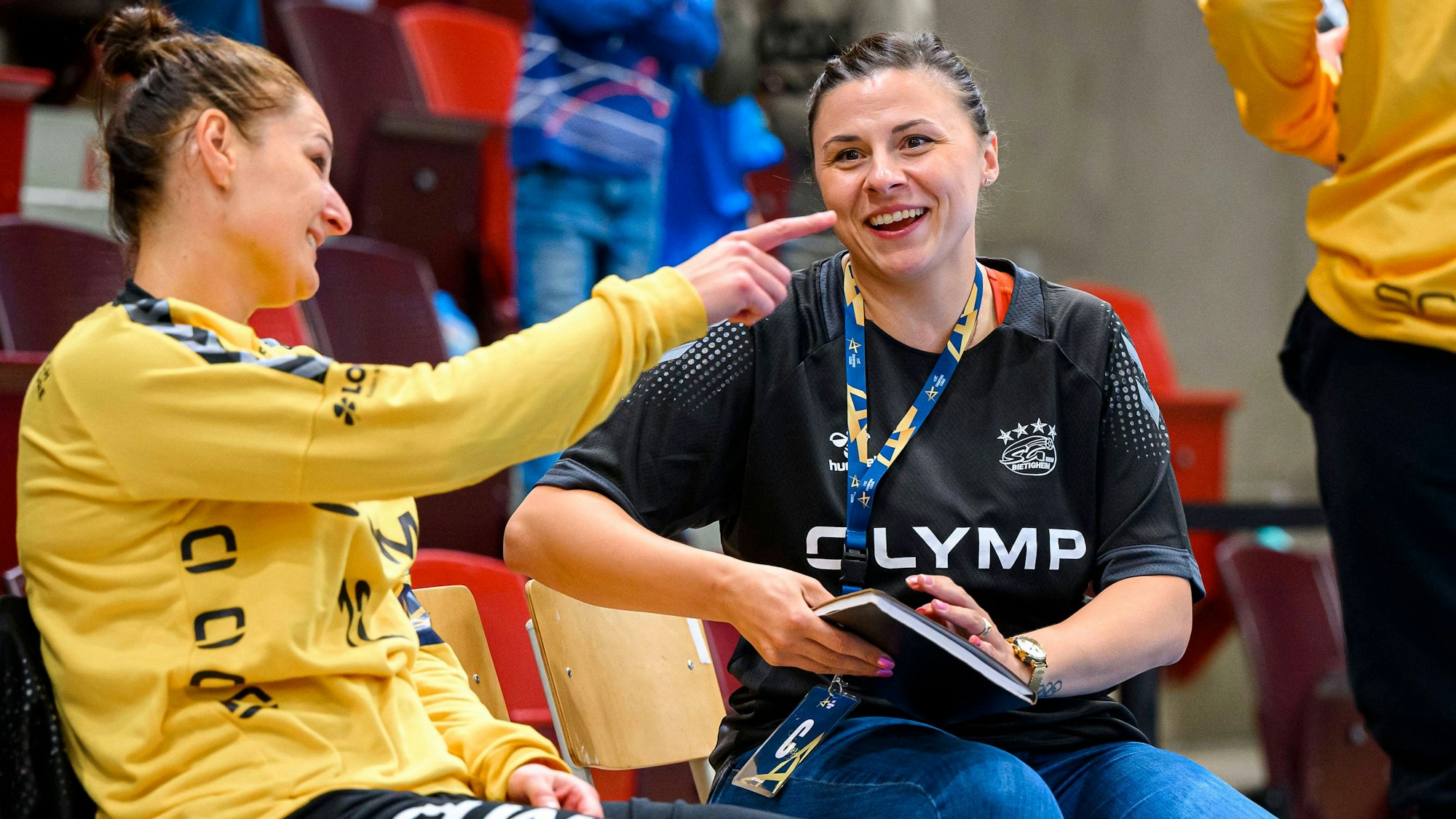 Jasmina Rebmann-Jankovic sitzt lachend neben der Bietigheimer Torhüterin Melinda Szikora, die ihr was erzählt.