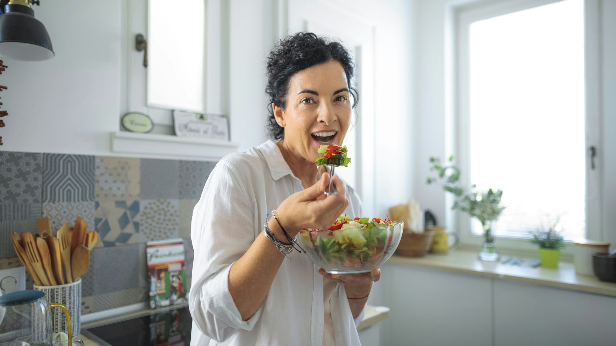 Eine Frau steht in einer Küche und isst Salat