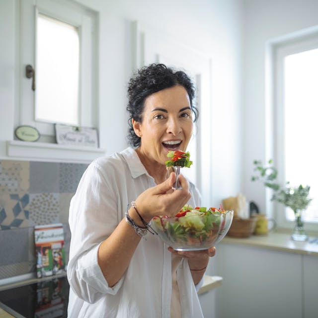 Eine Frau steht in einer Küche und isst Salat