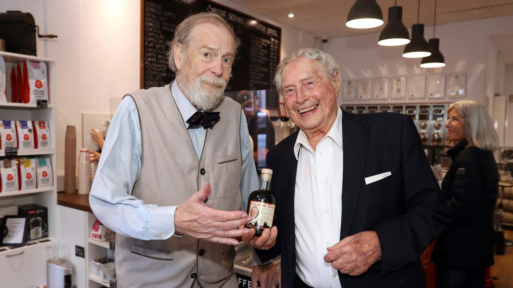 Philipp M. Laufenberg und Ludwig Sebus stehen nebeneinander und halten eine Likörflasche in die Kamera.